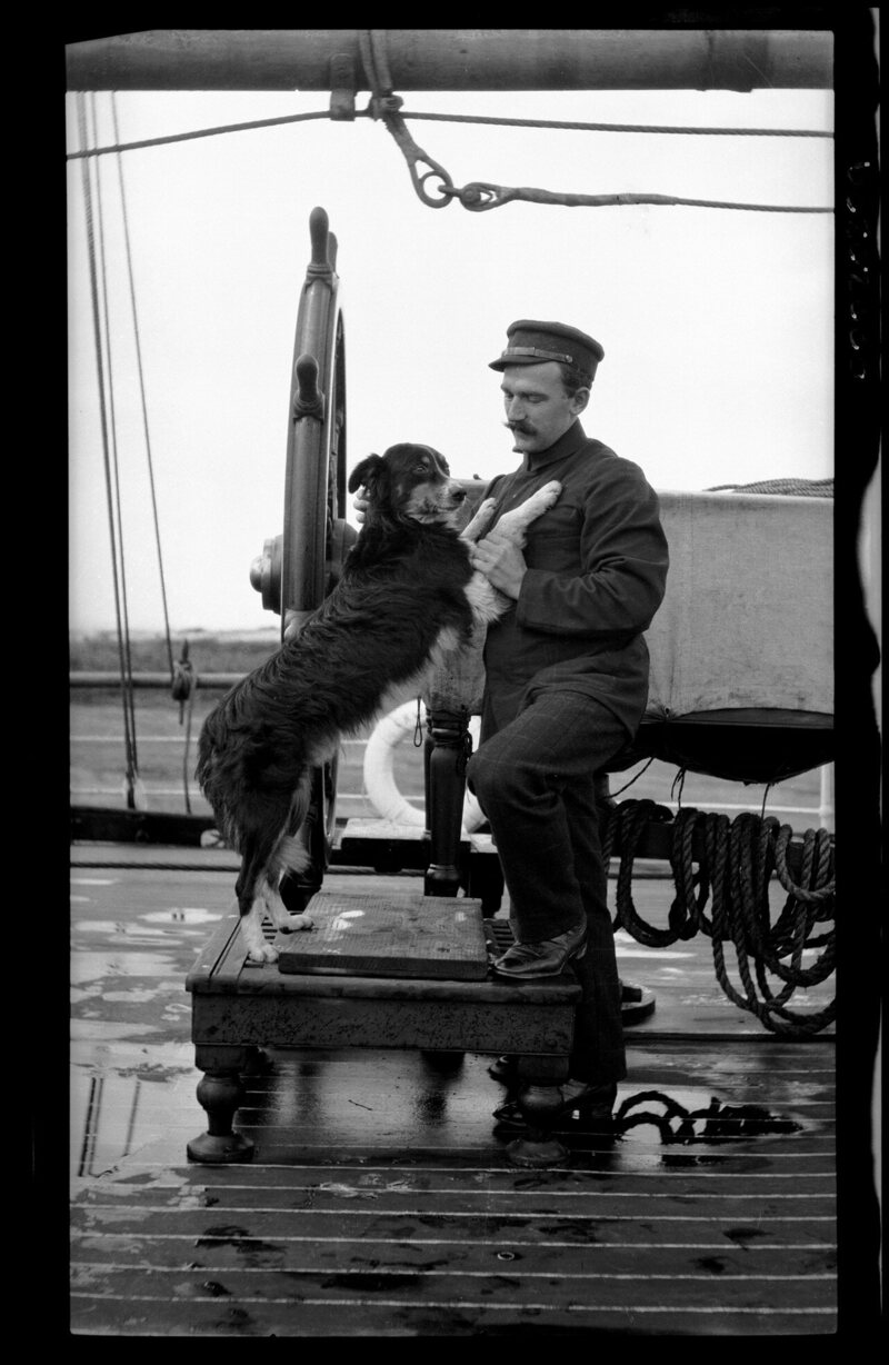 An Australian officer with a pet dog at the ship's wheel, 1907–28. 