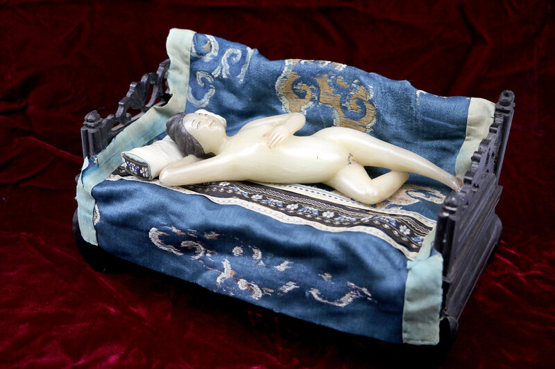A jade diagnostic doll rests on a tiny embroidered throw. 