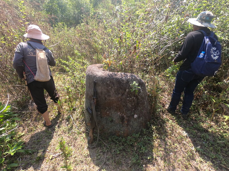 Two expedition members walk past a newly documented stone jar. 