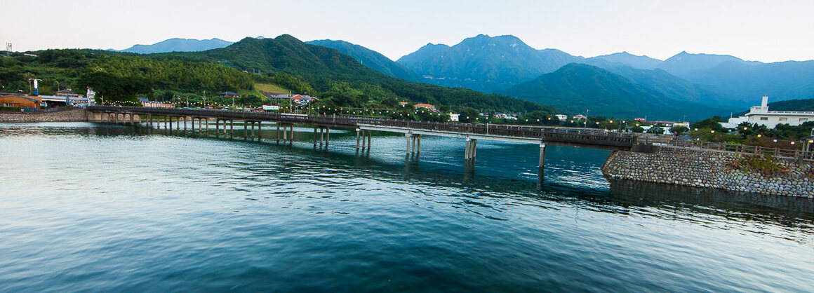 The undulating mountains at the center of the island serve as the backdrop for an archetypal Japanese lantern-covered wooden bridge at Miyanoura Port.