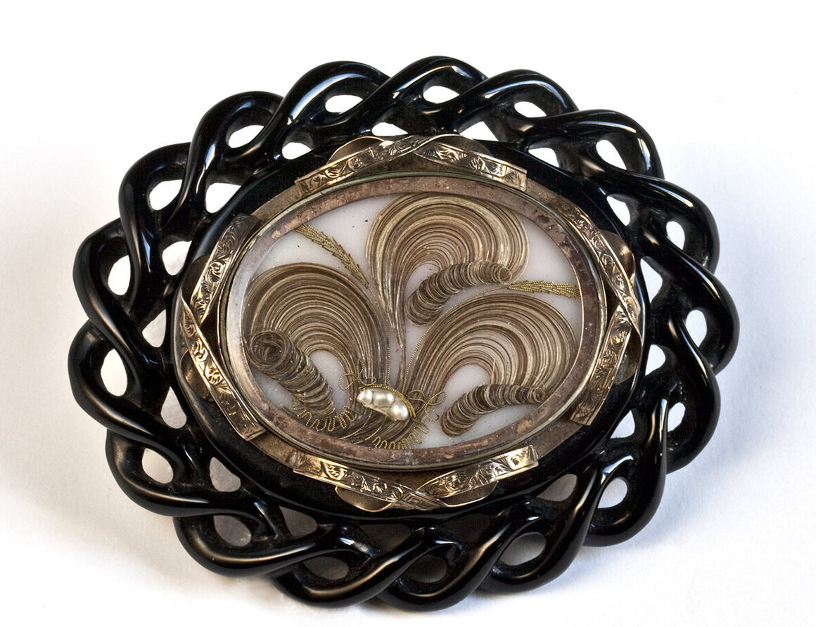 Brooch made of Whitby Jet, brass, glass, gold wire, seed pearls, and human hair using palette work, mid-19th century.